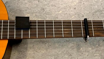Strengedæmeren sidder på den øverste del af guitaren og capo på den nederste. Strengedæmeren sidder på den øverste del af guitaren og capo på den nederste.